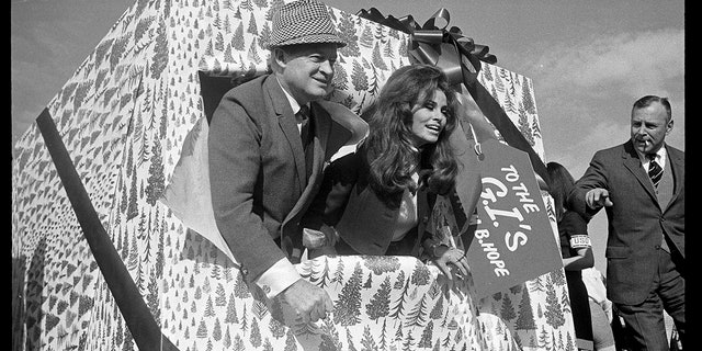 Comedian Bob Hope and actress Raquel Welch break through a decorated package labled "To the G.I.'s" moments before boarding a MATS airline as Hope and his troupe of 60 people departed on his 17th annual Christmas tour of overseas military bases on Dec. 15, 1967.