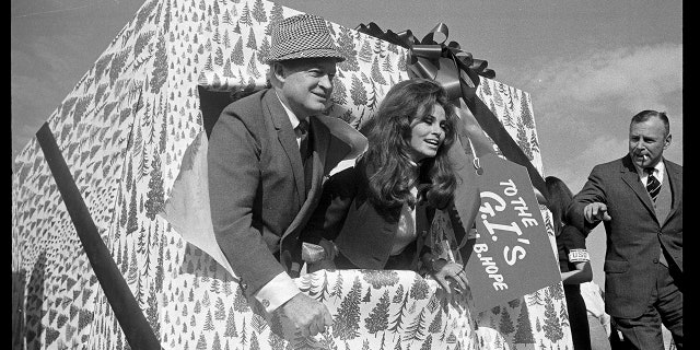 Comedian Bob Hope and actress Raquel Welch break through a decorated package labled "To the G.I.'s" moments before boarding a MATS airline as Hope and his troupe of 60 people departed on his 17th annual Christmas tour of overseas military bases on Dec. 15, 1967.