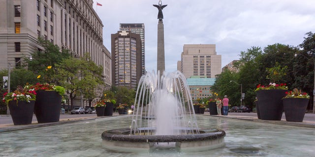 This file image shows a fountain by University Avenue in Toronto's downtown district, a famous place in a city square with large pots and commercial buildings. 