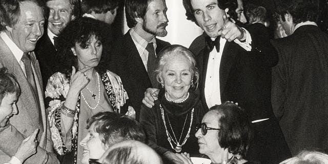 John Travolta, Travolta's mother, and producer Robert Stigwood (far left) at a premiere after-party for "Saturday Night Fever" in December 1977. In beard is British rock journalist Nik Cohn. The hit movie is based on what proved years later to be a fabricated magazine article by Cohn.