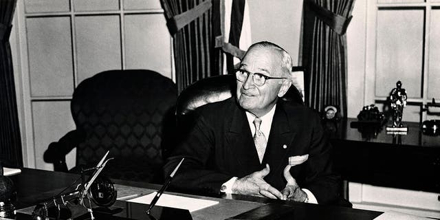 President Harry S. Truman seated in the White House with the sign 