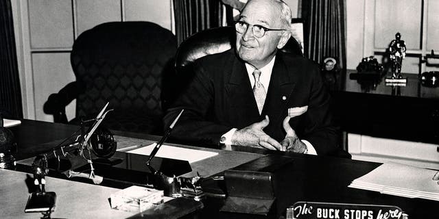 President Harry S. Truman seated in the White House with the sign 