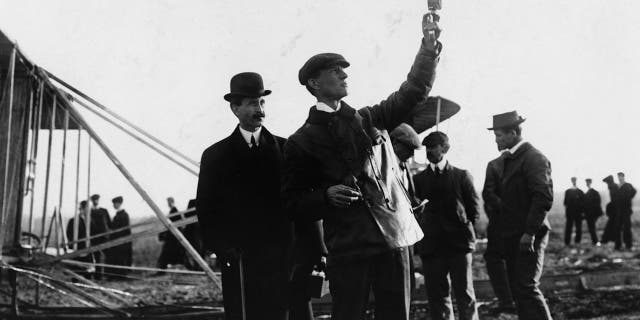 Picture of the Wright Brothers with Orville watching Wilbur take readings outdoors, circa 1908.