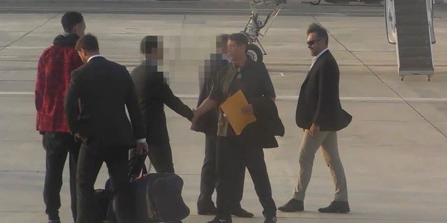 Brittney Griner, in red, on the tarmac as Viktor Bout, with the envelope, passes.