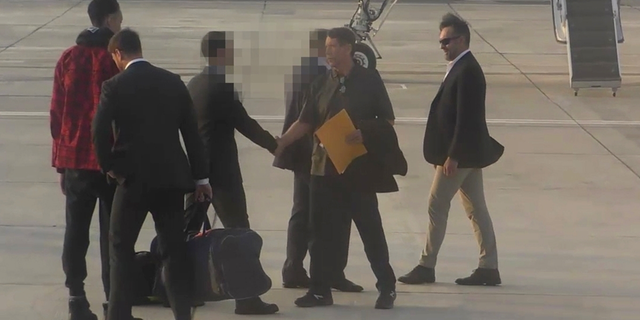 Brittney Griner, in red, on the tarmac as Viktor Bout, with the envelope, walks by.