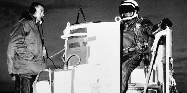 FILE - In this photo provided by the U.S. Air Force, Capt. Joseph Kittinger Jr., aerospace laboratory test director, sits in the open balloon gondola after his first parachute test jump for Project Excelsior at the Air Force Missile Development Center, N.M., Nov. 16, 1959. The gondola carried him at an altitude of 76,400 feet for his record free fall jump of more than 12 miles. At left is David Willard, who designed and developed special equipment for the gondola.