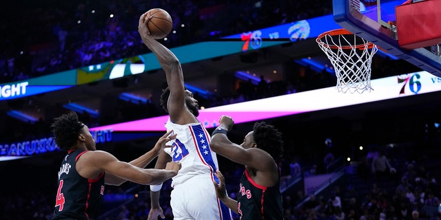 Philadelphia 76ers' Joel Embiid, center, goes up for a dunk against Toronto Raptors' Scottie Barnes, left, and O.G. Anunoby during the second half of an NBA basketball game, Monday, Dec. 19, 2022, in Philadelphia.