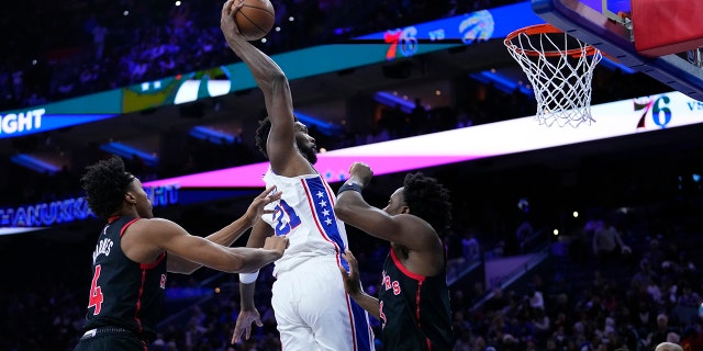 Philadelphia 76ers' Joel Embiid, center, goes up for a dunk against Toronto Raptors' Scottie Barnes, left, and O.G. Anunoby during the second half of an NBA basketball game, Monday, Dec. 19, 2022, in Philadelphia.