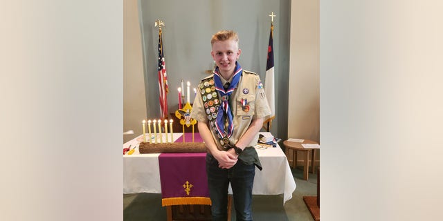 Ken DeLand smiles in Eagle Scout uniform in front of church alter. 