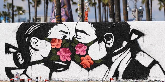 Palm trees stand behind a street art piece by artist Pony Wave depicting two people kissing while wearing face masks on Venice Beach on March 21, 2020, in Venice, California.