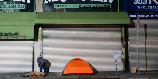A homeless man stands next to his tent in Los Angeles, Wednesday, Dec. 14, 2022.