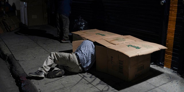 David Hernandez, a 62-year-old homeless man, crawls into his bed made with cardboard boxes in Los Angeles, late Wednesday, Dec. 14, 2022. 