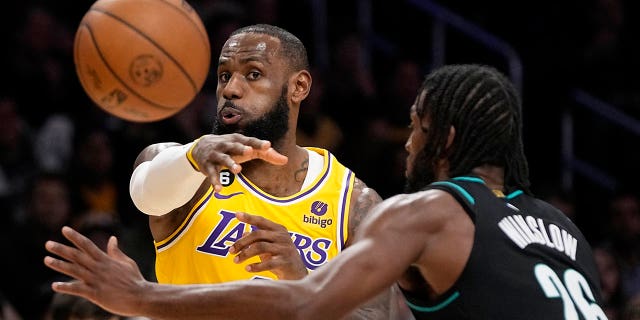 El alero de los Lakers de Los Ángeles, LeBron James, a la izquierda, pasa el balón mientras el alero de los Trail Blazers de Portland, Justise Winslow, defiende durante la primera mitad de un partido de baloncesto de la NBA el miércoles, 30 de noviembre de 2022 en Los Ángeles. 