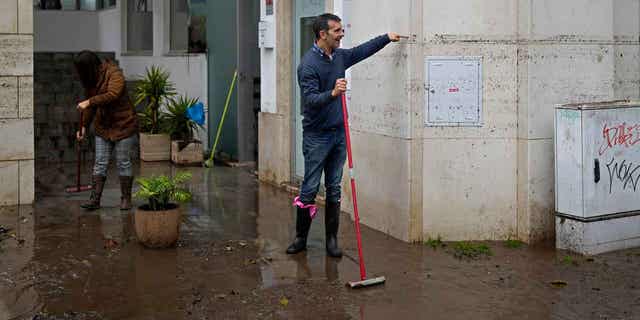 A man sweeping water from a building shows the height that the water reached when the street was flooded overnight in Alges, Portugal, on Dec. 13, 2022. 