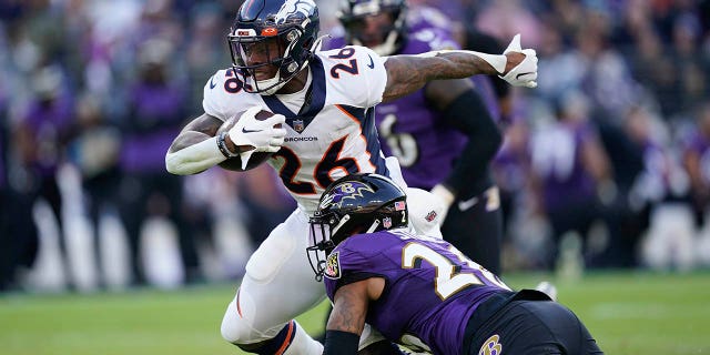 Denver Broncos running back Mike Boone (26) comes under pressure from Baltimore Ravens safety Geno Stone (26) as he carries the ball in the second half of an NFL football game, Sunday, Dec. 4, 2022, in Baltimore.