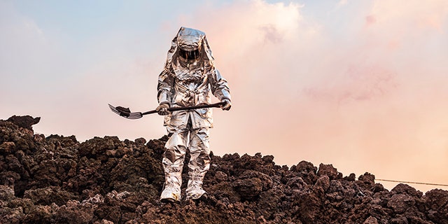 Wearing a protective suit, Armando Salazar steps carefully across sizzling rock, carrying a chunk of glowing lava on a pitchfork.