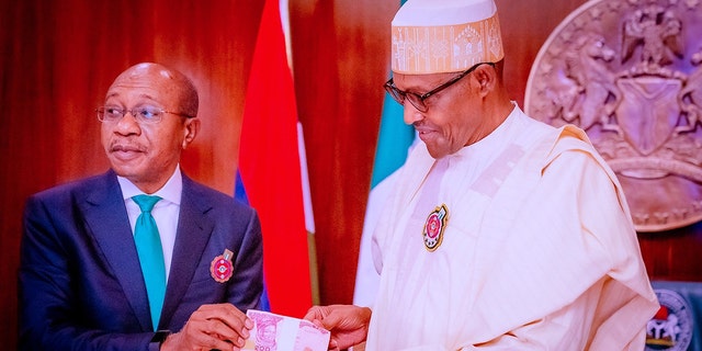ФАЙЛ: Годвін Емефеле, ліворуч, президент Центрального банку Нігерії (CBN), відвідує презентацію нових банкнот після того, як президент Нігерії Мухаммаду Бухарі, праворуч, оприлюднив банкноти нового дизайну через підробку та посилення проблем безпеки 23 листопада 2022 року, в Абуджі, Нігерія.