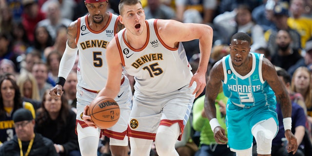 Denver Nuggets center Nikola Jokic, front, picks up a loose ball as guard Kentavious Caldwell-Pope, back left, and Charlotte Hornets guard Terry Rozier pursue in the first half of an NBA basketball game, Sunday, Dec. 18, 2022, in Denver. 