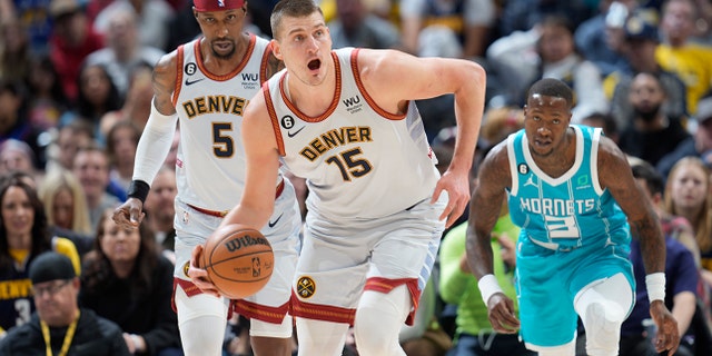 Denver Nuggets center Nikola Jokic, front, picks up a loose ball as guard Kentavious Caldwell-Pope, back left, and Charlotte Hornets guard Terry Rozier pursue in the first half of an NBA basketball game, Sunday, Dec. 18, 2022, in Denver.