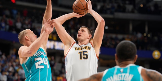 El pívot de los Denver Nuggets, Nikola Jokic, al centro, lanza un tiro entre el pívot de los Charlotte Hornets, Mason Plumlee, a la izquierda, y el alero PJ Washington, en la primera mitad de un partido de baloncesto de la NBA, el domingo 18 de diciembre de 2022 en Denver. 