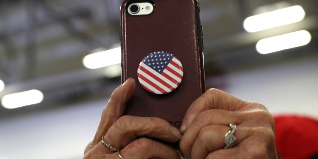 A woman holds a phone adorned with a Stars and Stripes PopSocket.