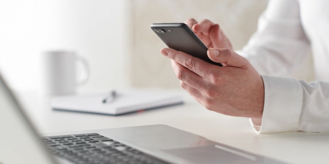 Close-up detail of a businessman working on a smartphone and laptop at his desk, shot on January 31, 2019. 