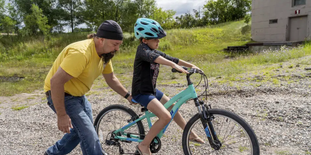 Steven Pringle, owner of Build a Bicycle - Bicycle Therapy, helps Kadence Horton, 8, of Iron River learn to ride her new bike outside his shop in Kingsford, in Michigan's Upper Peninsula, on Friday, July 29, 2022.