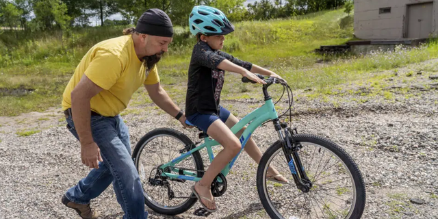 Steven Pringle, owner of Build a Bicycle - Bicycle Therapy, helps Kadence Horton, 8, of Iron River learn to ride her new bike outside his shop in Kingsford, in Michigan's Upper Peninsula, on Friday, July 29, 2022.