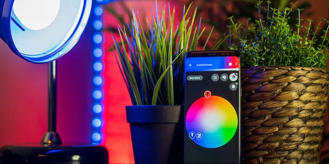 An LED lamp on a tabletop with a smartphone displaying the controls to customize color and brightness.
