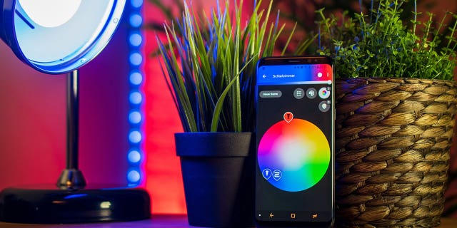 An LED lamp on a tabletop with a smartphone displaying the controls to customize color and brightness.