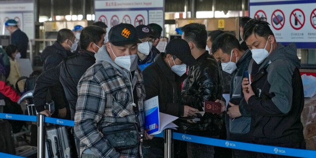 Masked travelers check their passports while queuing at the international flight check-in counter at Beijing Capital International Airport in Beijing, Thursday, March 27, 2022. 