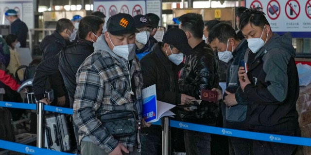 Masked travelers check their passports as they line up at the international flight check in counter at the Beijing Capital International Airport in Beijing, Thursday, Dec. 29, 2022.