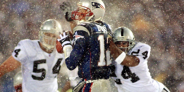 New England Patriots quarterback Tom Brady takes a hit from Charles Woodson of the Oakland Raiders on a pass attempt in the last two minutes of the game in their AFC playoff January 19, 2002 in Foxboro, Massachusetts.