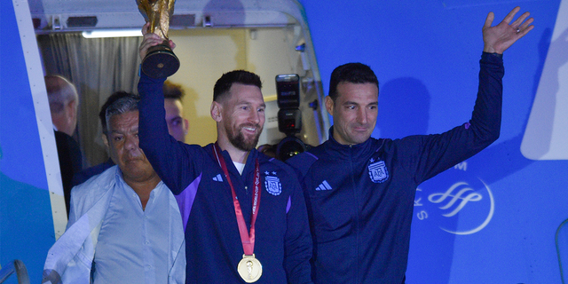 Argentina's Lionel Messi holds the FIFA World Cup trophy as he deplanes, with coach Lionel Scaloni, in Buenos Aires, Argentina.