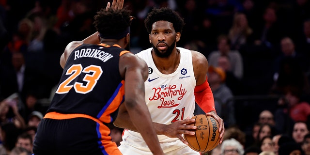 Philadelphia 76ers center Joel Embiid (21) looks to pass around New York Knicks center Mitchell Robinson during the first half of an NBA basketball game, Sunday, Dec. 25, 2022, in New York. 