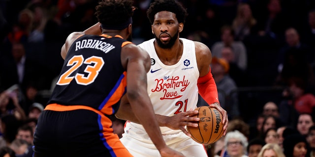 Philadelphia 76ers center Joel Embiid (21) looks to pass around New York Knicks center Mitchell Robinson during the first half of an NBA basketball game, Sunday, Dec. 25, 2022, in New York.