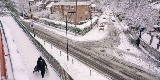 A woman pulls a shopping trolley, in a snow covered residential area in Leytonstone, in London, Monday, Dec. 12, 2022. Snow and ice have swept across parts of the UK, with cold wintry conditions set to continue for days. 