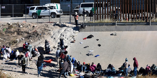 FILE - Migrants wait to cross the U.S.-Mexico border from Ciudad Juárez, Mexico, next to U.S. Border Patrol vehicles in El Paso, Texas, Wednesday, Dec. 14, 2022. A federal judge on Thursday temporarily blocked the Biden administration from ending a Trump-era policy requiring asylum-seekers to wait in Mexico for hearings in U.S. immigration court.