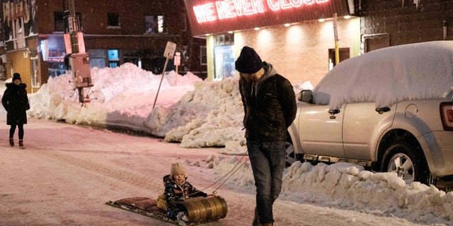 A family walks past Cameron's 24 Hour Store in Buffalo, New York, on December 26, 2022. - Emergency crews in New York were scrambling on December 26, 2022, to rescue marooned residents from what authorities called the "blizzard of the century," a relentless storm that has left at least 25 dead in the state and is causing US Christmas travel chaos. 