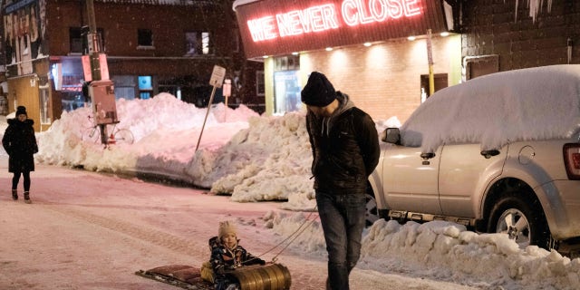 TOPSHOT - A family walks past Cameron's 24 Hour Store in Buffalo, New York, on December 26, 2022. - Emergency crews in New York were scrambling on December 26, 2022, to rescue marooned residents from what authorities called the "blizzard of the century," a relentless storm that has left at least 25 dead in the state and is causing US Christmas travel chaos. (Photo by Joed Viera / AFP) (Photo by JOED VIERA/AFP via Getty Images)