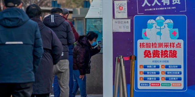 A woman shows her health check QR code as residents line up to get their routine COVID-19 throat swabs at a coronavirus testing site, Dec. 7, 2022.
