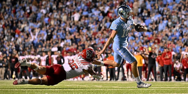 Drake Maye (10) of the North Carolina Tar Heels breaks away from Drake Thomas (32) of the North Carolina State Wolfpack for a touchdown during the first half of a game at Kenan Memorial Stadium Nov. 25, 2022, in Chapel Hill, N.C. The Wolfpack won 30-27 in overtime. 