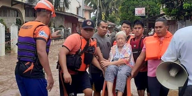 An elderly woman sits on a chair while being carried by coast guard personnel wading through floodwaters in the southern Philippines on Dec. 26, 2022. 