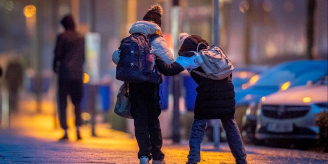 School children help each other on the way to school in icy conditions when rain fell on a frosted surface in Frankfurt, Germany, early Monday, Dec. 19, 2022.