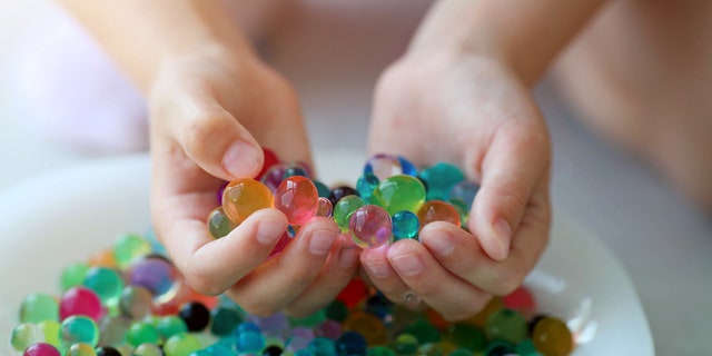 A young person is shown holding an array of orbeez or hydrogel water balls. 