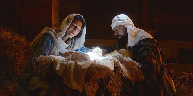 A reenactment of Mary and Joseph as they caress the baby Jesus sleeping in a manger under bright divine light after the child's birth in Bethlehem.