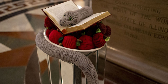 A crocheted snake and apples and a book by Copernicus on Dec. 6, 2022, make up the seasonal display placed by members of the Satanic Temple of Illinois at the Illinois State Capitol. (Brian Cassella/Chicago Tribune/Tribune News Service via Getty Images) 