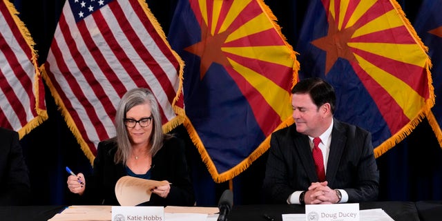 Katie Hobbs, the Democratic governor-elect and current secretary of state, left, signs the official certification for the Arizona general election canvass as Arizona Republican Gov. Doug Ducey, right, looks on during a ceremony at the Arizona Capitol in Phoenix, Monday, Dec. 5, 2022.
