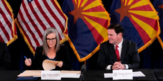 Katie Hobbs, the Democratic governor-elect and current secretary of state, left, signs the official certification for the Arizona general election canvass as Arizona Republican Gov. Doug Ducey, right, looks on during a ceremony at the Arizona Capitol in Phoenix, Monday, Dec. 5, 2022.