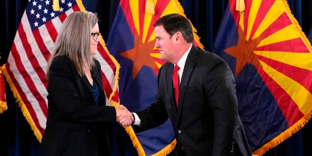 Katie Hobbs, the Democratic governor-elect and current secretary of state, left, shakes hands with Republican Gov.  Doug Ducey after she signed the official certification for the Arizona general election canvas during a ceremony at the Arizona Capitol in Phoenix, Dec. 5, 2022.